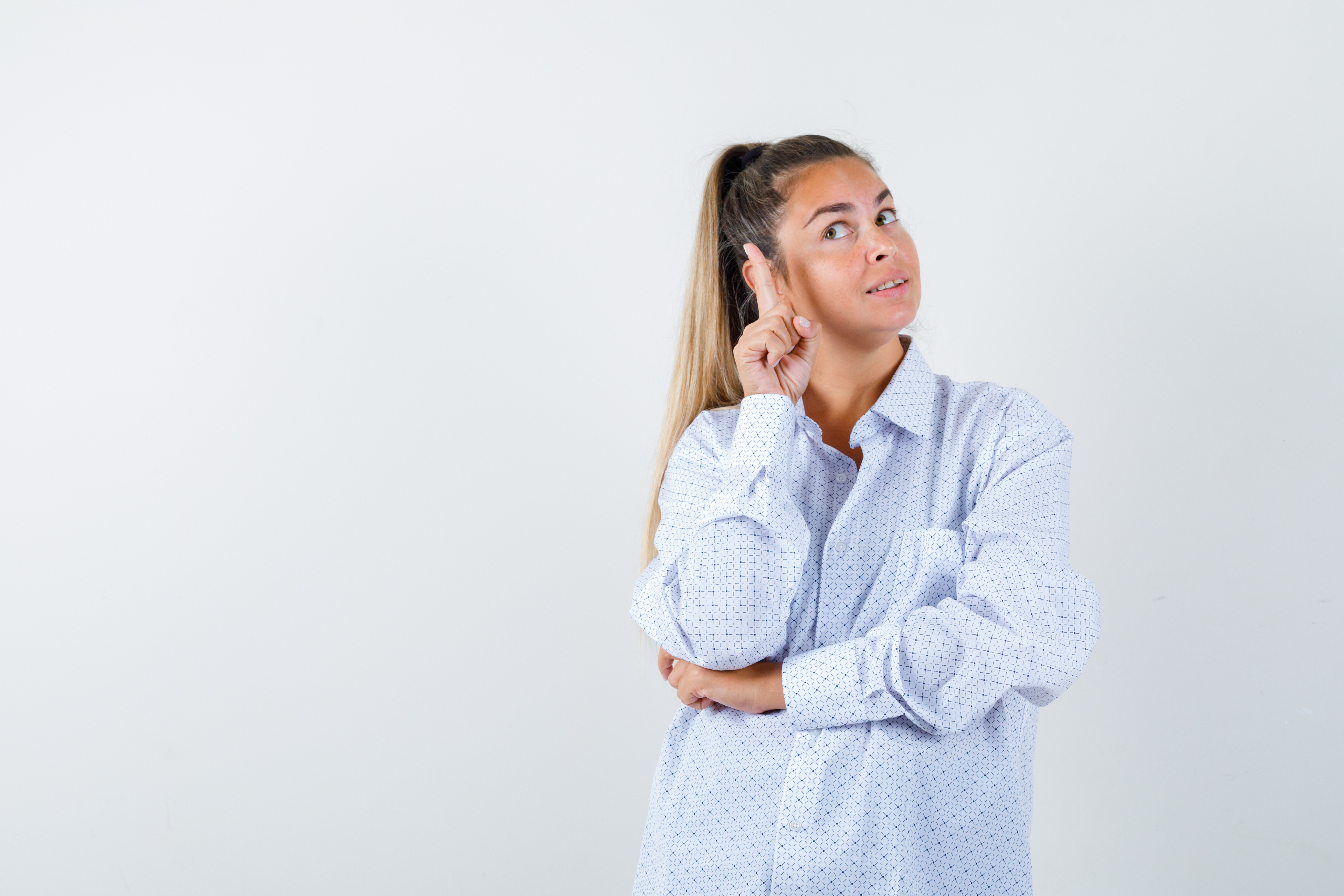 Mujer joven con camisa blanca apuntando hacia la derecha con el dedo